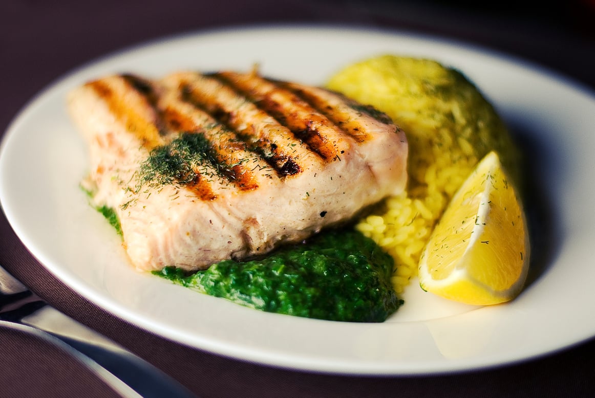 Close-up Photography of Grilled Fish Meat With Green Porridge and Sliced Lemon on Round White Ceramic Plate